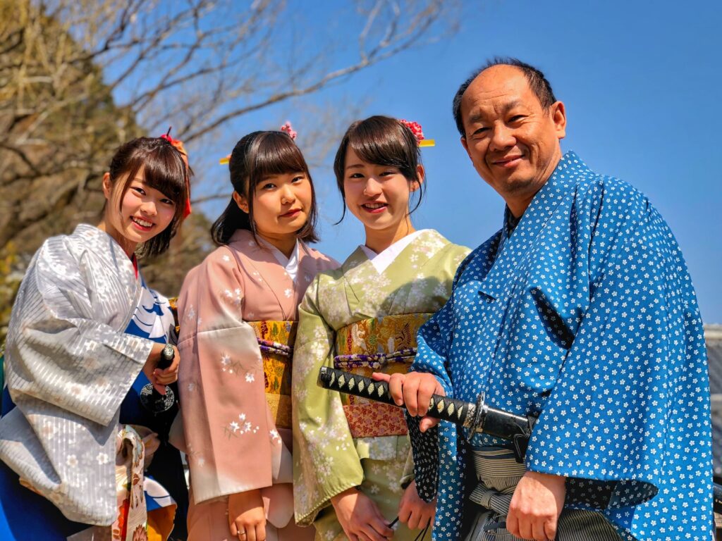 three women wearing kimono beside man holding katana sword