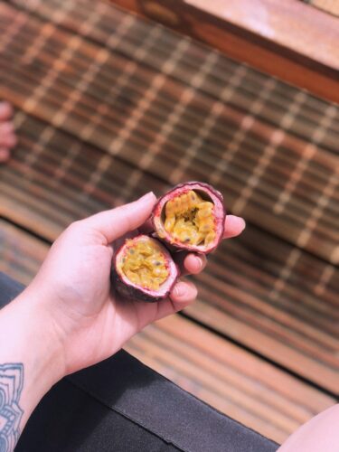 From above of crop anonymous tattooed female holding halved exotic ripe passion fruit in hand