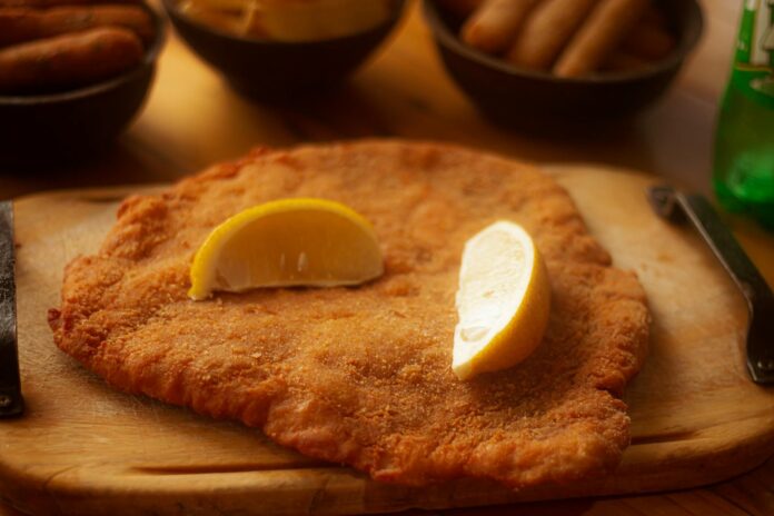 Cotoletta alla milanese dorata con spicchio di limone su tagliere
