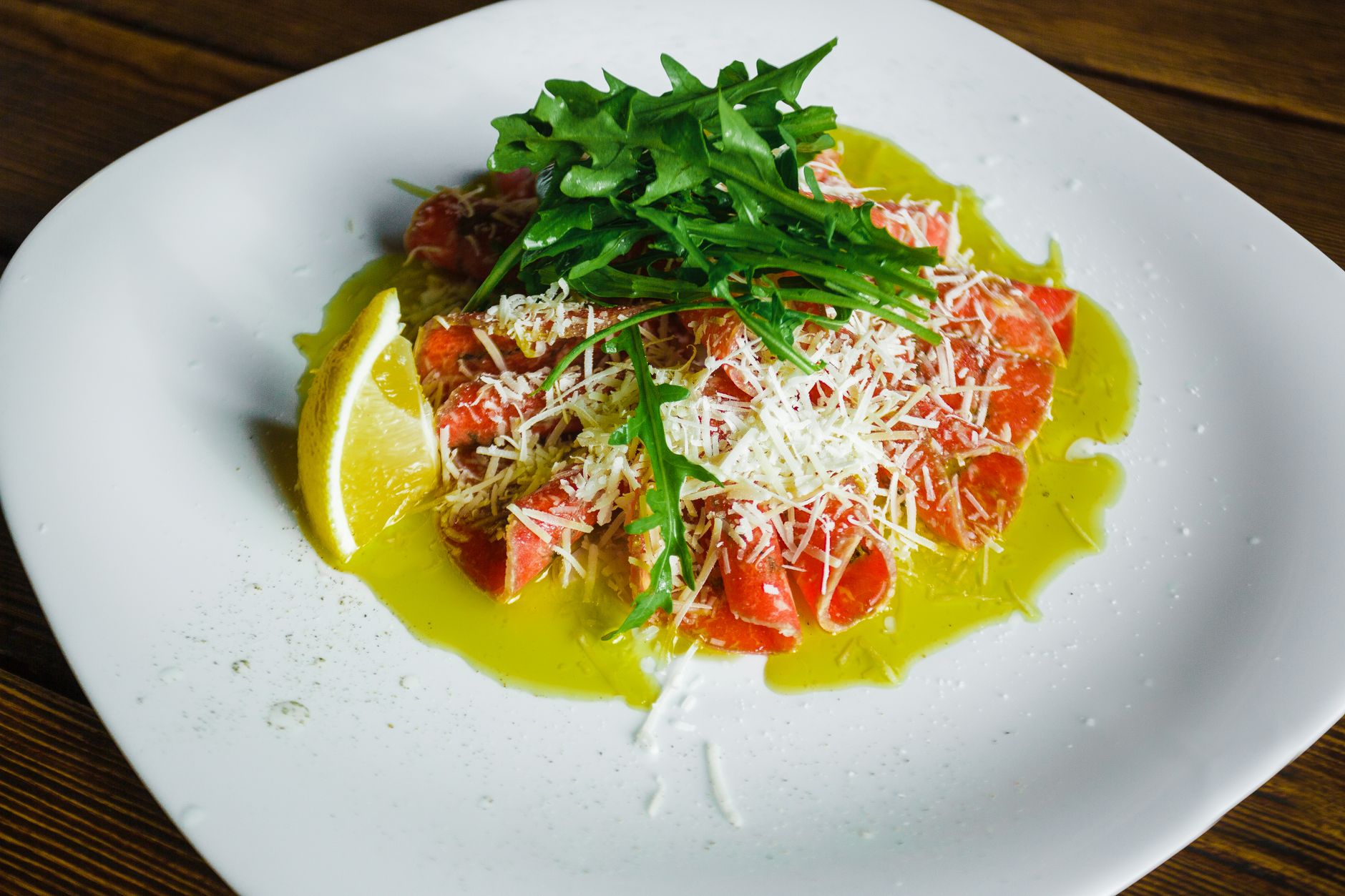 Piatto di carpaccio guarnito con olio, limone e scaglie di formaggio