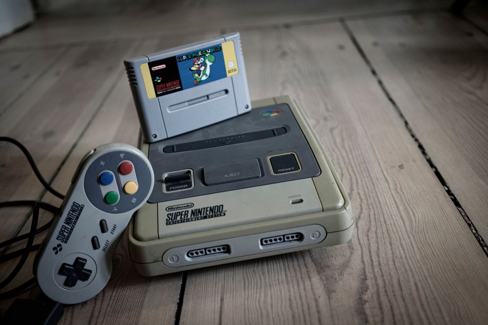 Vecchia console per videogiochi con cassetta inserita e controller sul pavimento