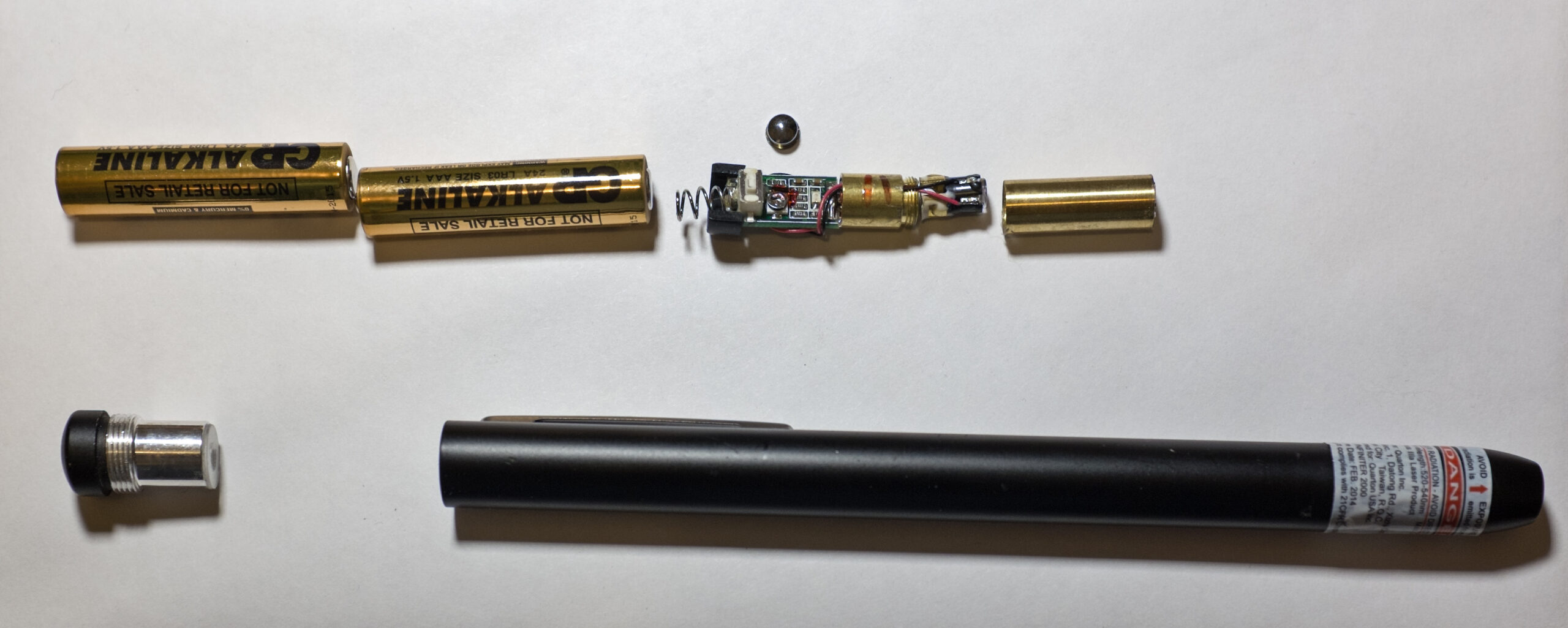 Puntatore laser verde smontato, con i componenti allineati sul piano