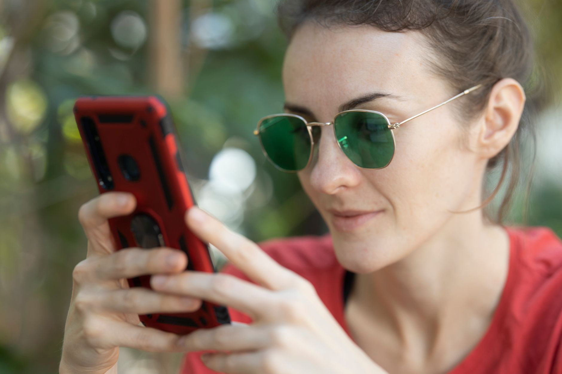 Donna con occhiali da sole che guarda lo schermo dello smartphone alla luce del giorno