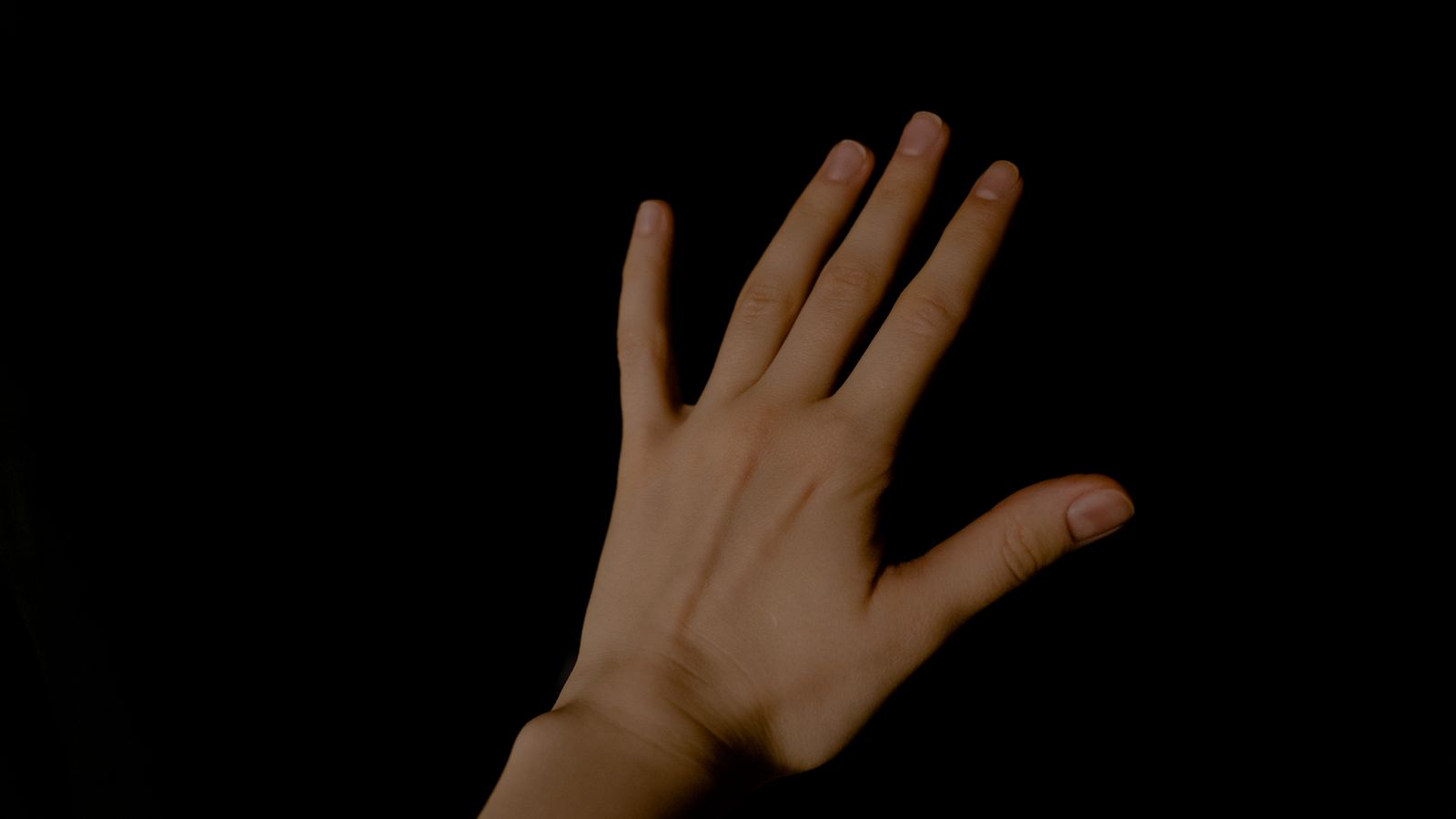 Primo piano di una mano umana con le dita distese su sfondo scuro
