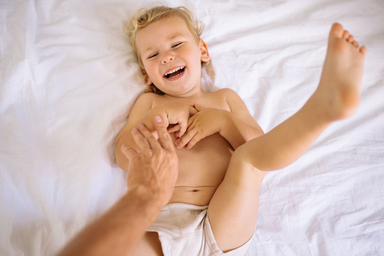 Un bambino ride mentre qualcuno gli fa il solletico sul letto