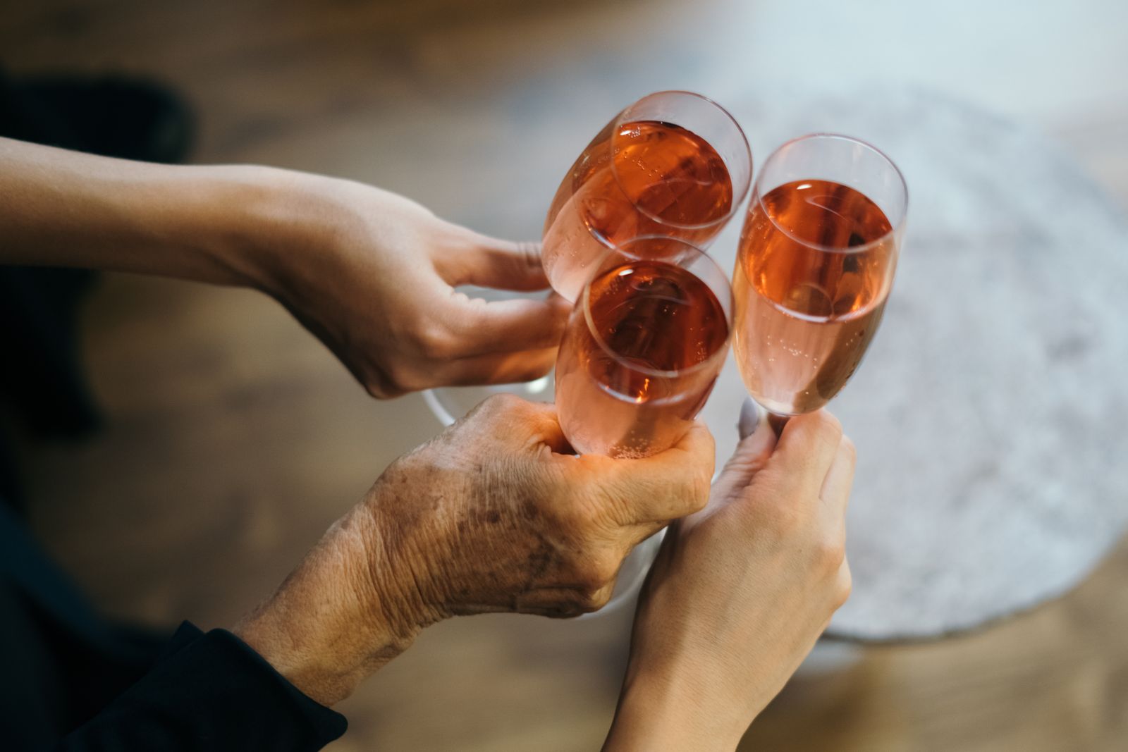 Tre mani che fanno tintinnare calici di spumante rosato in un brindisi