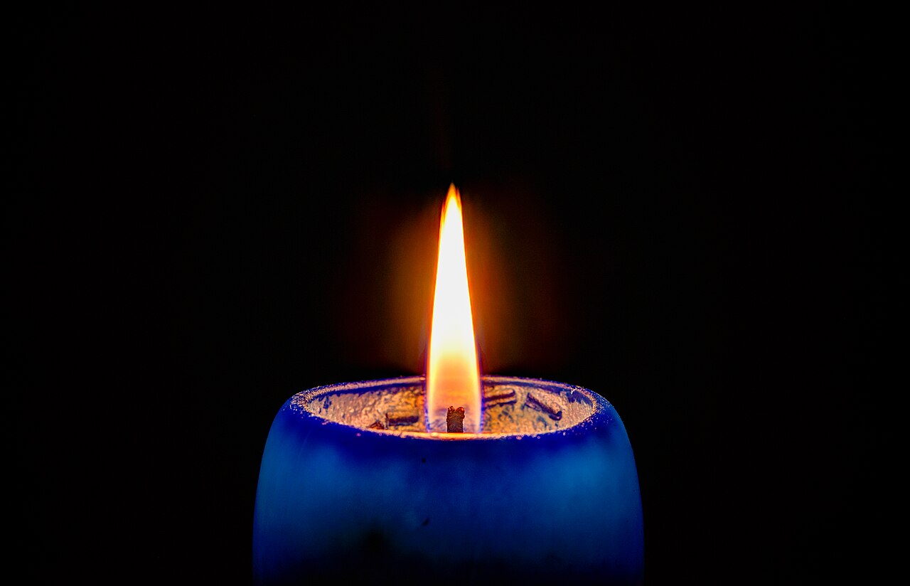 La fiamma gialla di una candela accesa su sfondo scuro